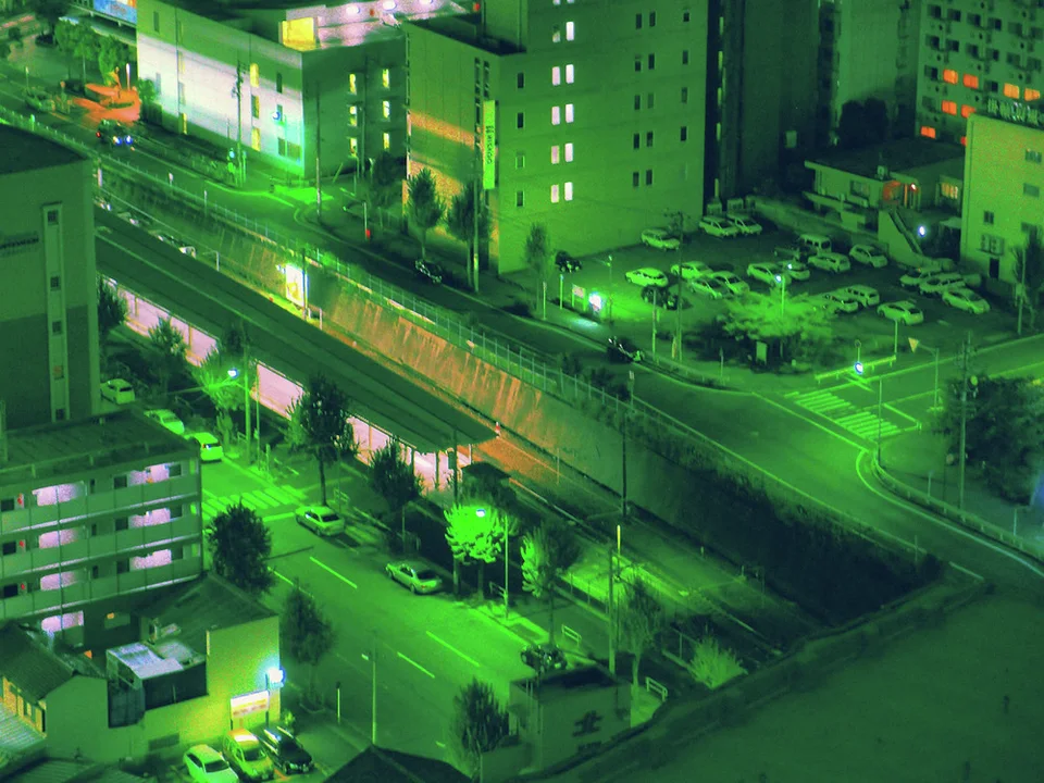 Green light washes over an elevated roadway, adjacent buildings and streets with elongated vehicle light trails.