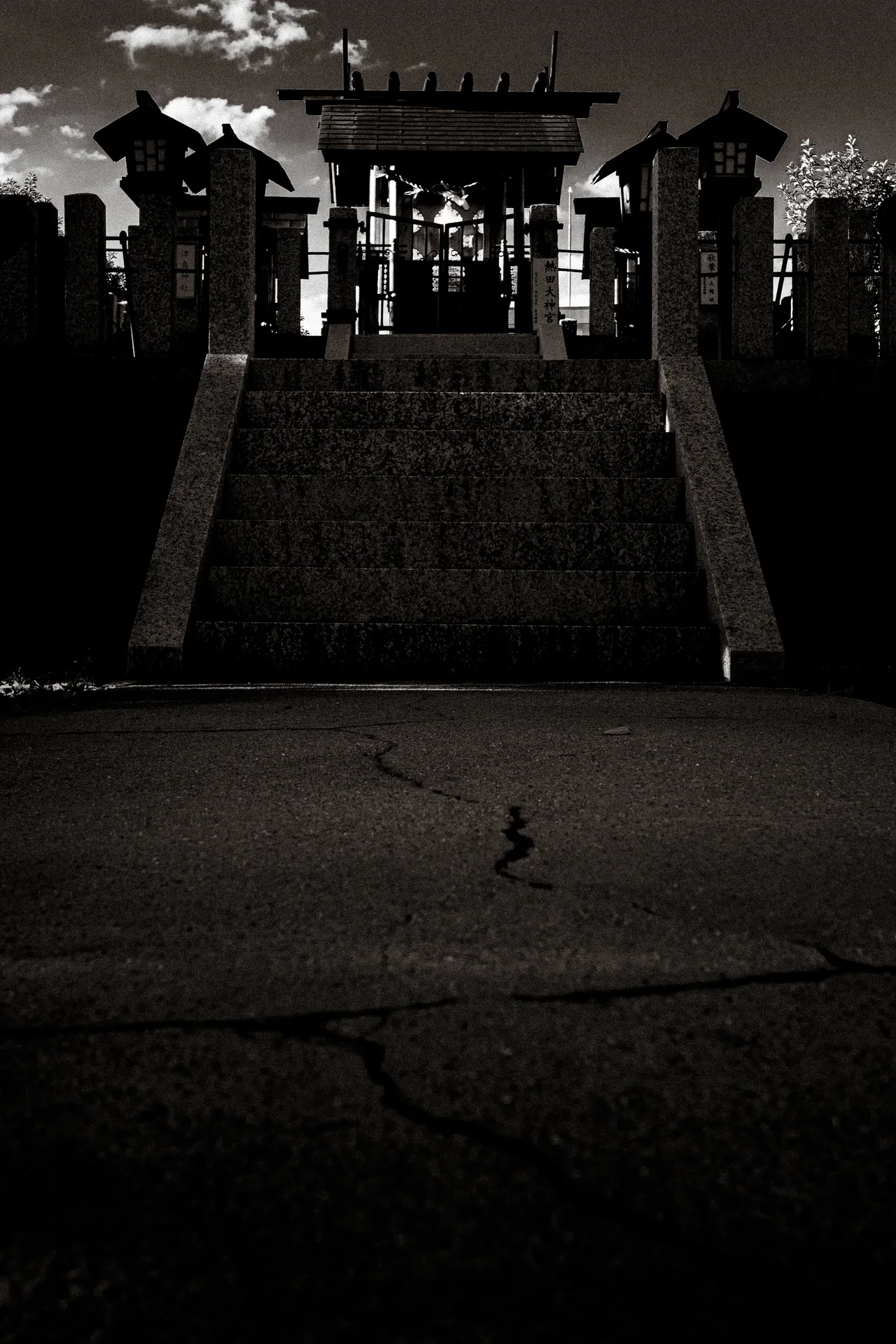 Stone steps lead toward a small shrine flanked by stone pillars in monochrome.
