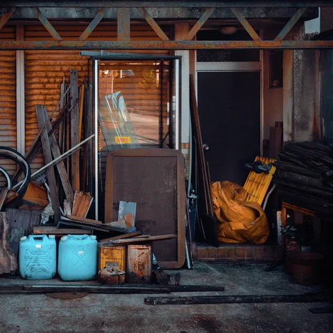 Blue containers and yellow sacks sit among timber and tools outside an open shed.