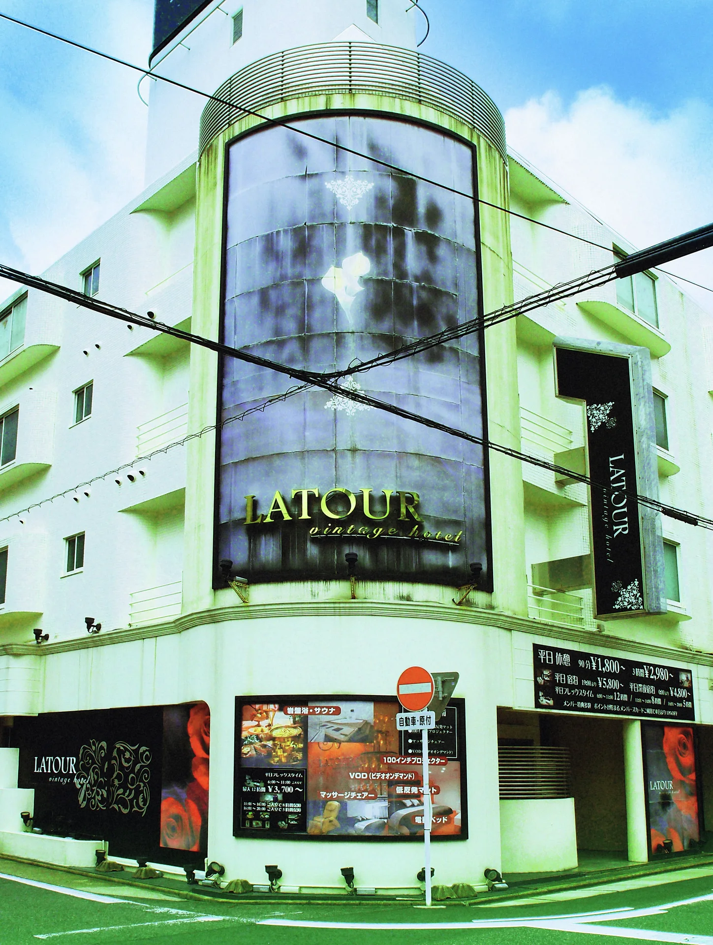 A rounded glass tower rises above a corner storefront beneath blue sky and crossing wires.