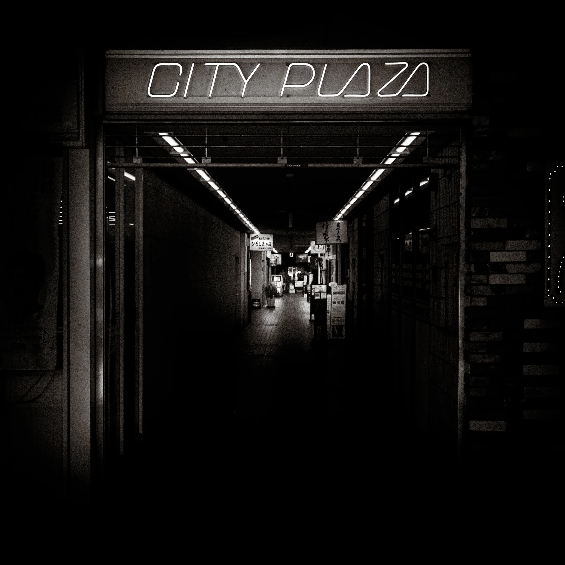 An illuminated City Plaza sign marks a dark corridor lined with ceiling lights in black and white.