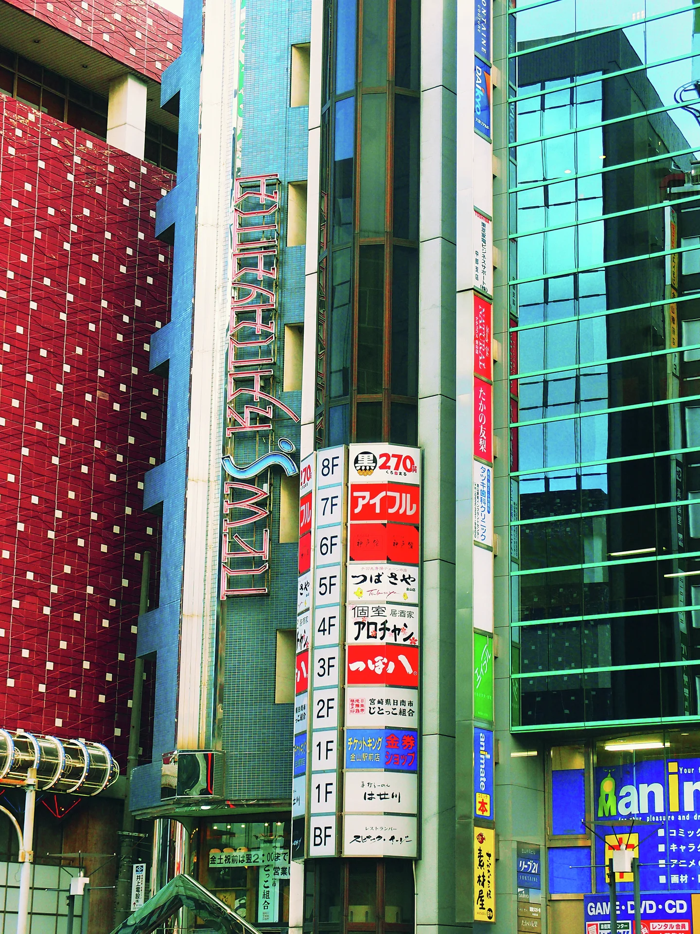A vertical column of colorful business signs stands between a red dotted facade and blue-green windows.