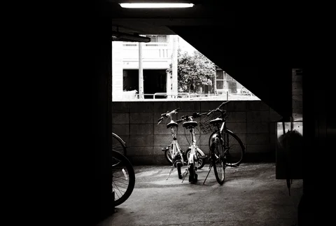 Bicycles stand within a dark covered passage illuminated by a triangular patch of daylight.