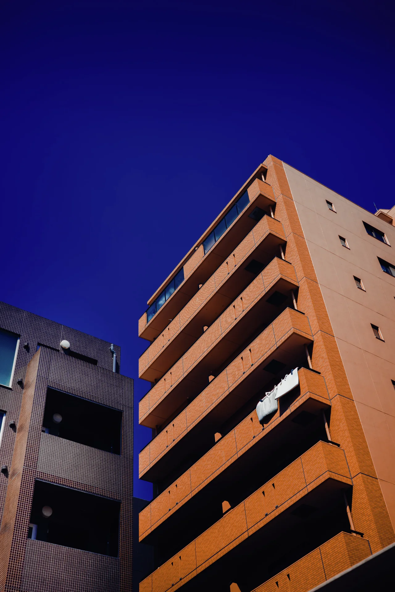 Repeating dark balconies project from an orange apartment building against a deep blue sky.