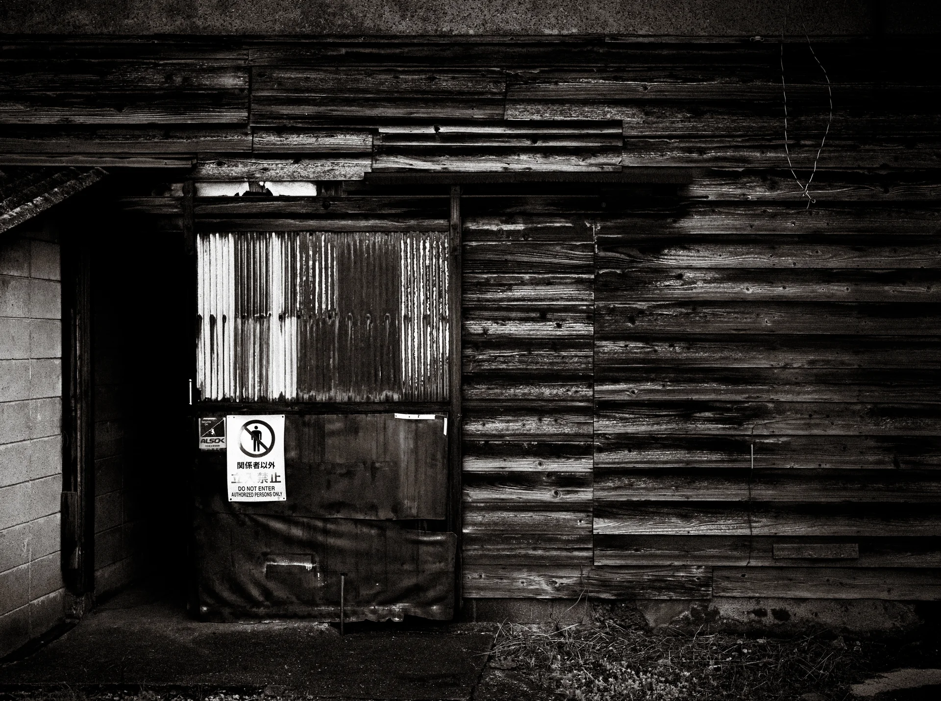 A patched doorway interrupts a deeply weathered horizontal wooden wall in black and white.