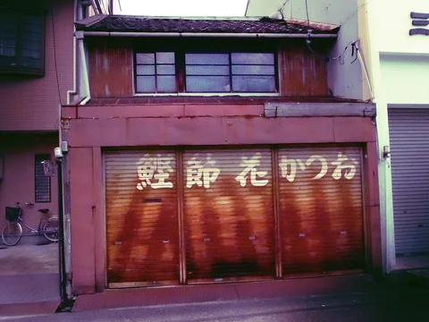 White characters span reddish closed shutters beneath weathered upper windows and a tiled roof.