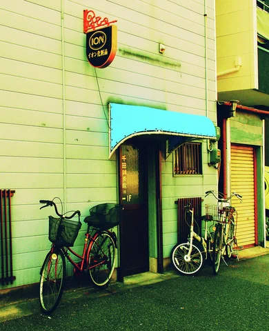 Bicycles flank a narrow doorway beneath a turquoise canopy on a pale paneled wall.