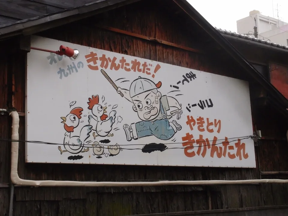 Cartoon chickens and a cook decorate a pale restaurant sign attached to dark wooden siding.