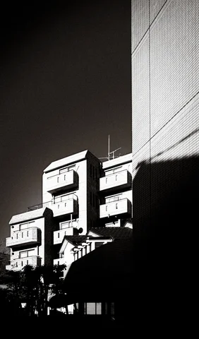 Rows of small metal boxes catch sunlight along a wall crossed by deep shadows in black and white.
