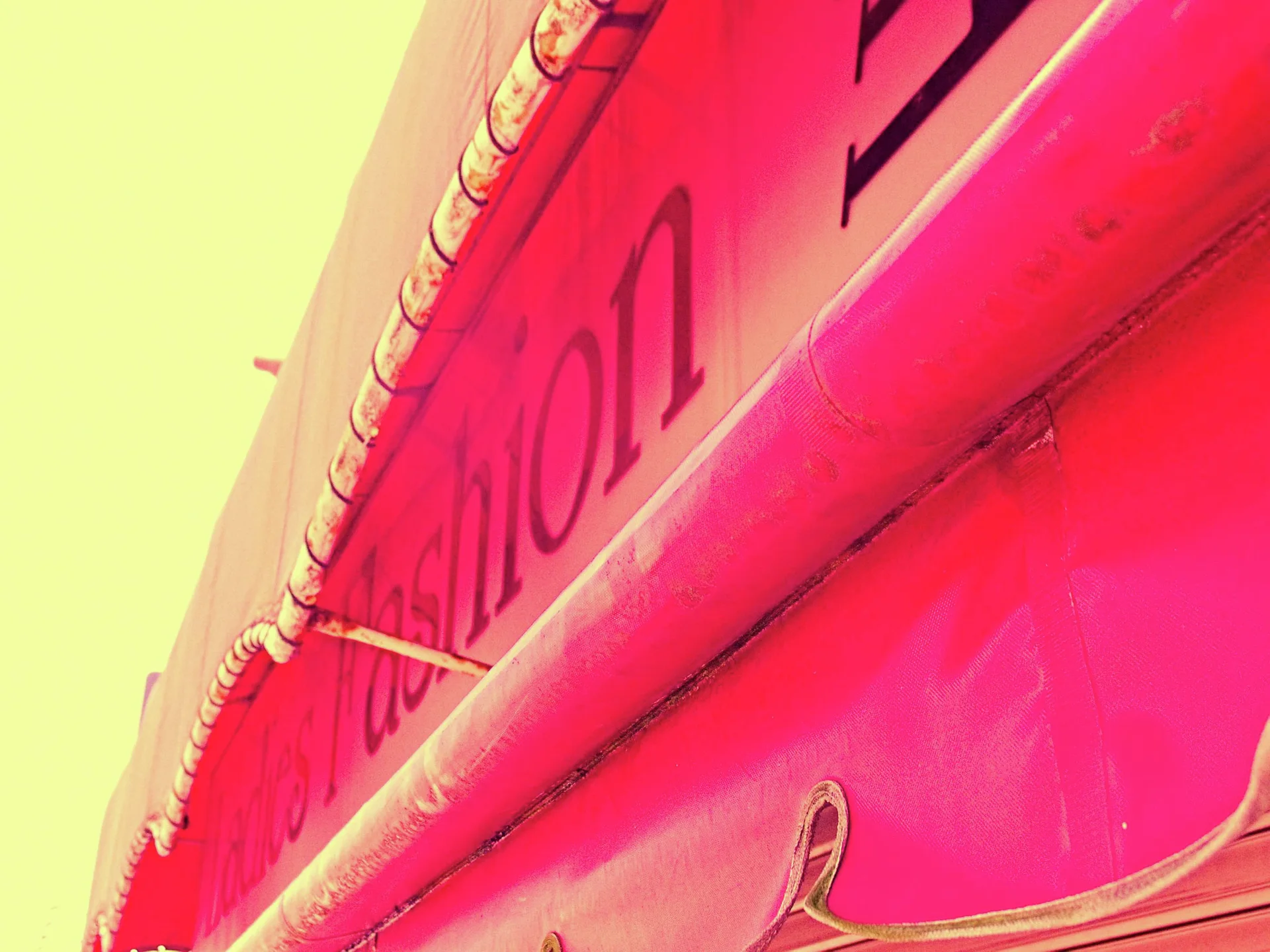 Dark lettering curves along a vivid red storefront fascia viewed steeply upward against a yellow sky.