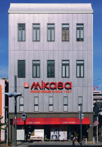 Repeated narrow windows line a tall pale facade above red lettering and a red ground-floor awning.