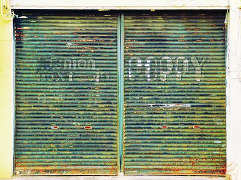 Faded white COPY lettering spans two rust-streaked green metal shutters in a pale frame.