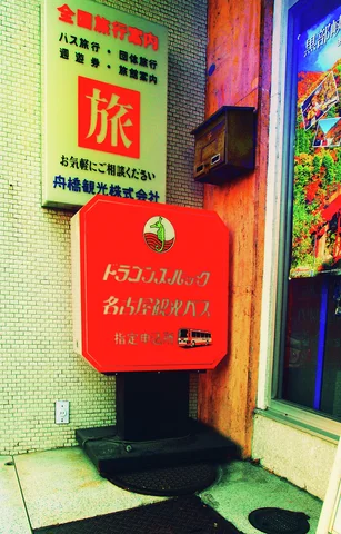 A bright red sign box stands beside a wooden post and colorful storefront posters.