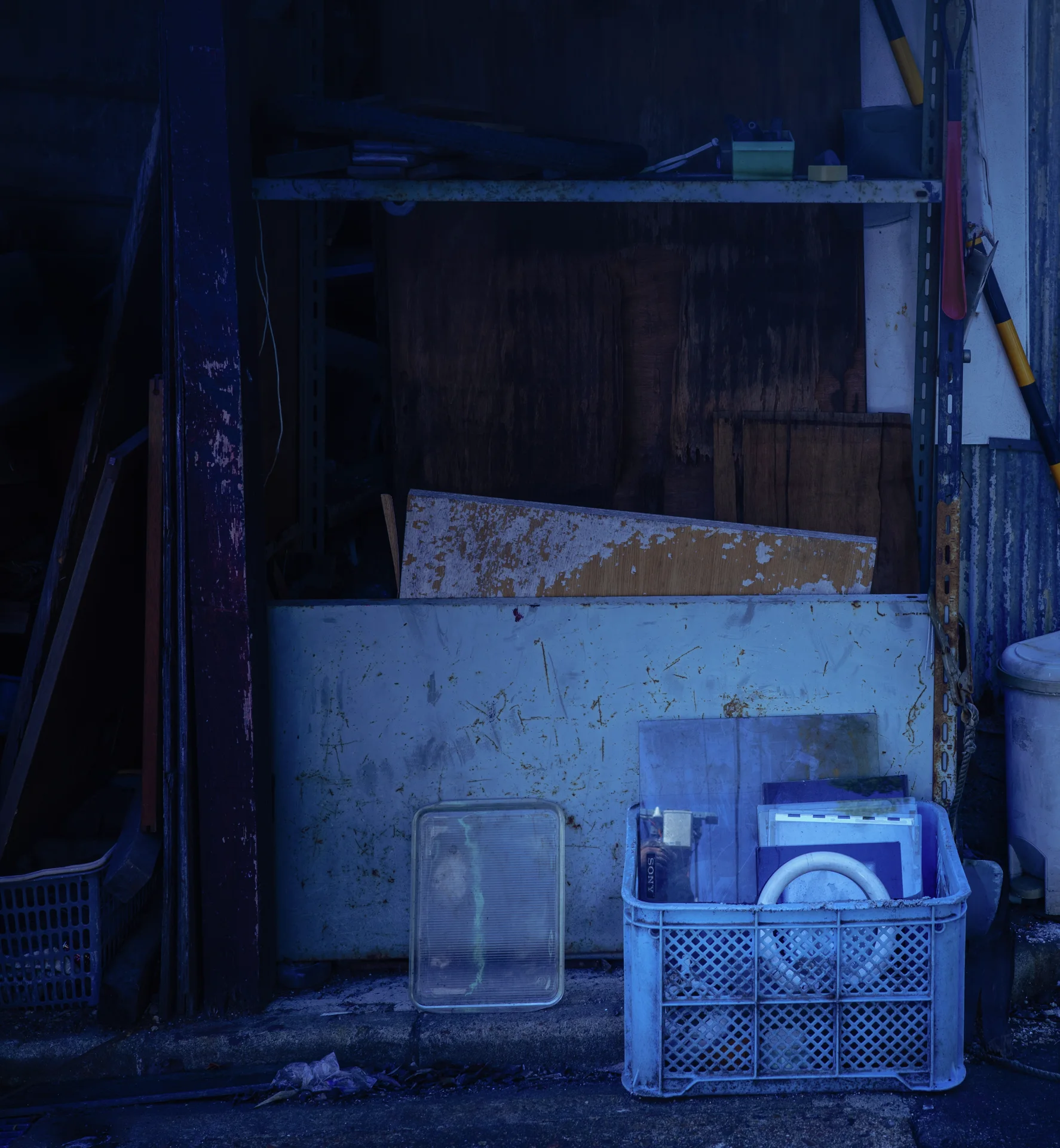 A blue plastic crate holds dishes before weathered boards in a shadowy entrance.