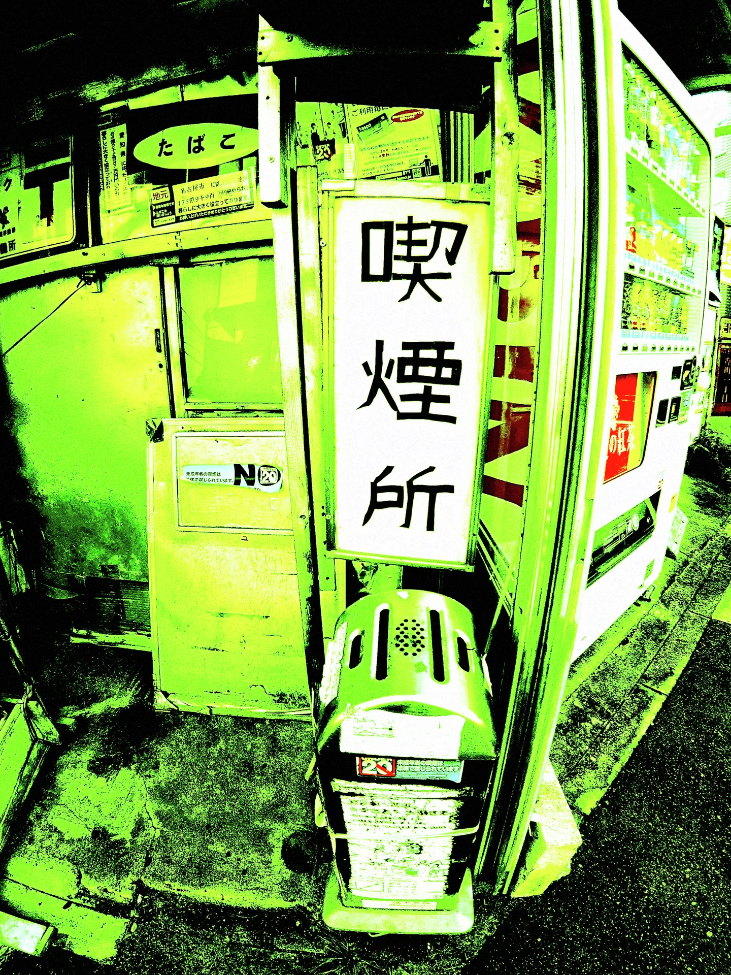 A tall white Japanese sign stands above a small container beside a vending machine and yellow wall.