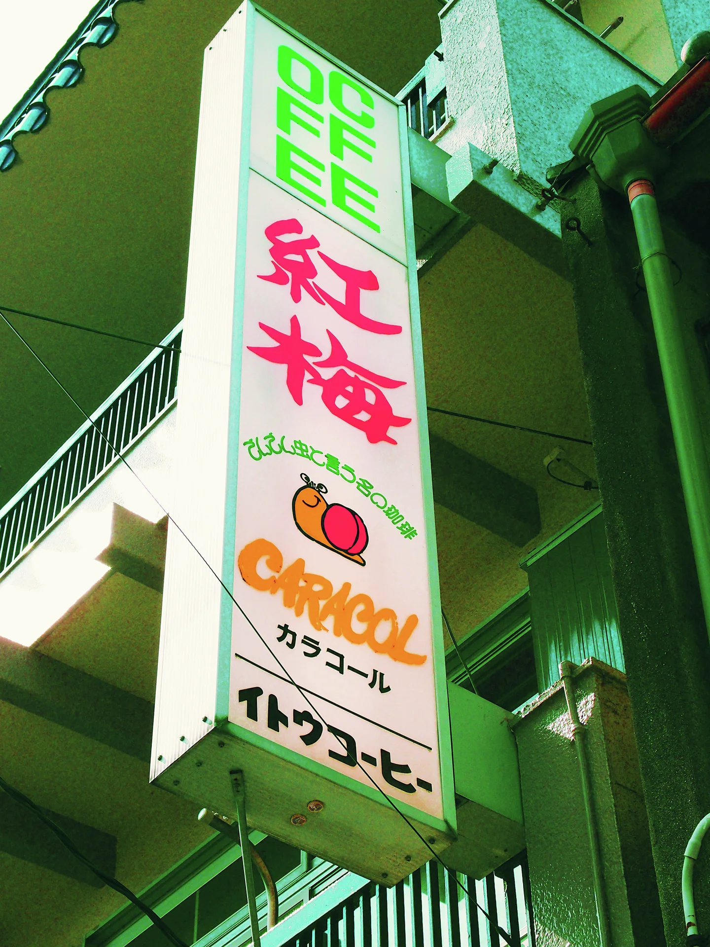 A tall white cafe sign with colorful lettering hangs beside concrete balconies and stairs.