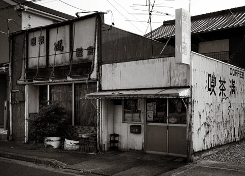 Faded coffee shop lettering covers an aging corner building with peeling walls and small entrances.