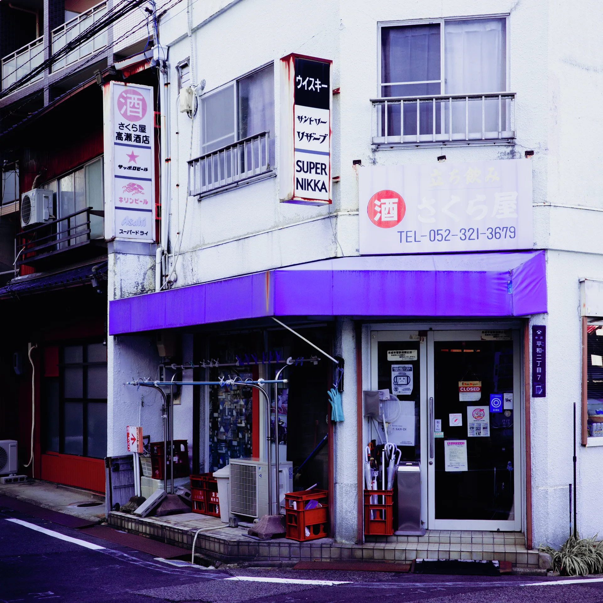A white corner storefront has a broad purple awning beneath upper windows and projecting narrow signs.