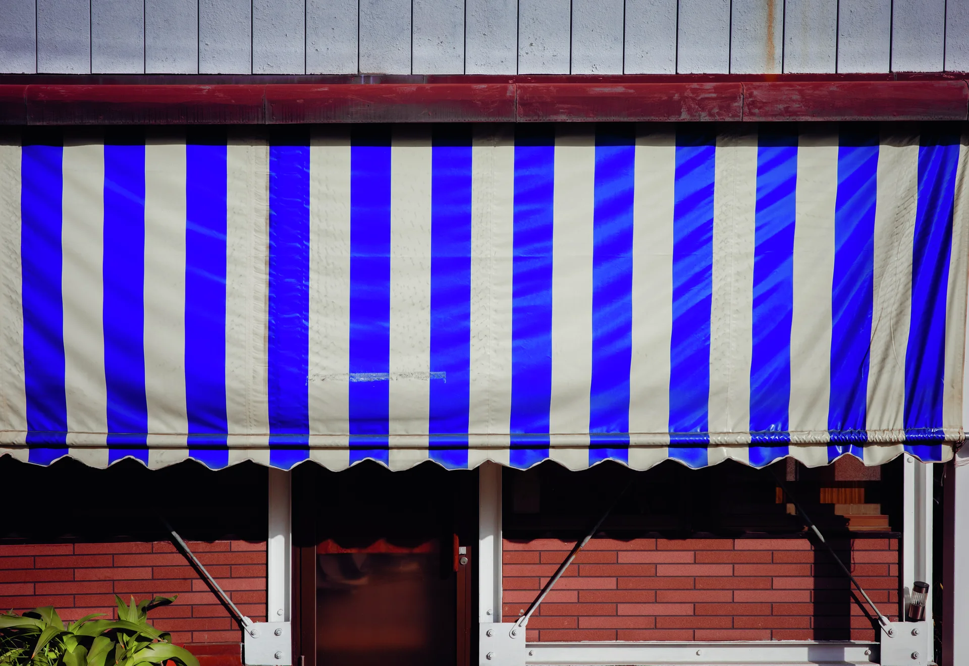 A blue-and-white striped awning stretches across a red brick storefront above a dark doorway.