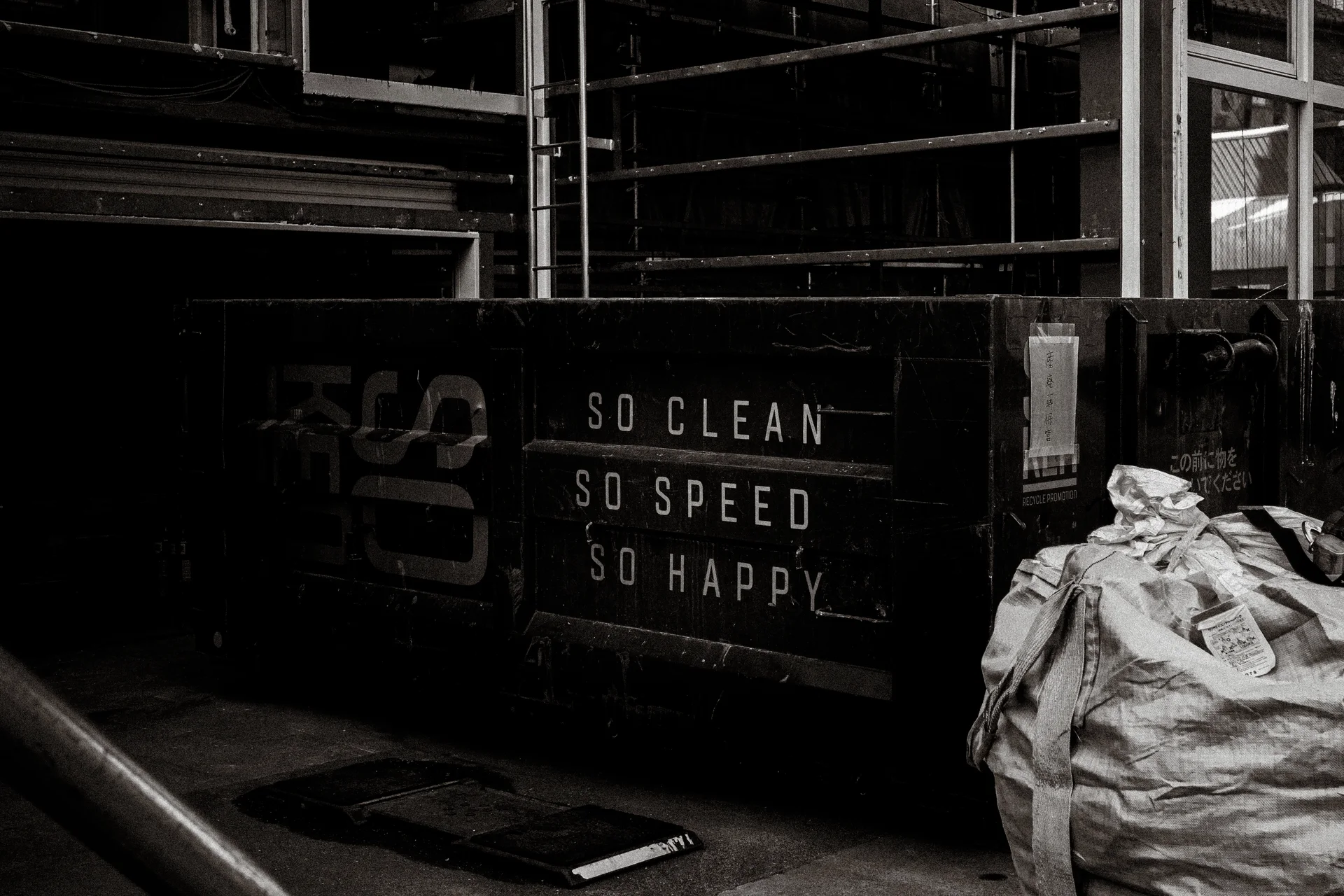 White English lettering covers a dark wall beside a large crumpled sack in black and white.