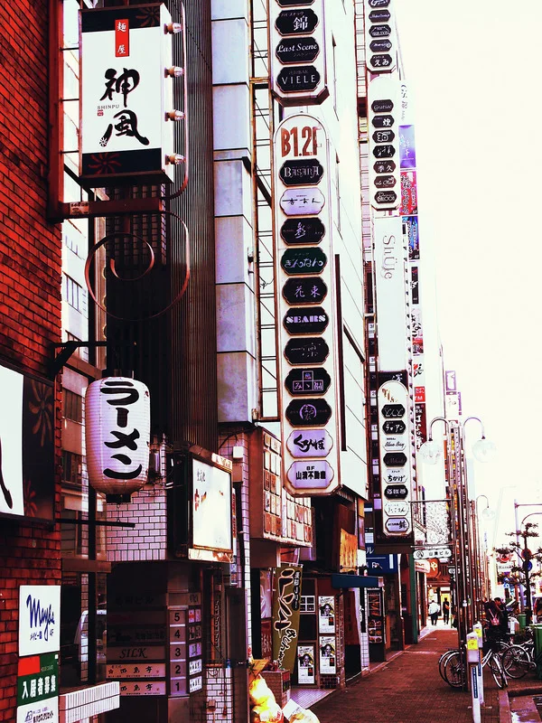 A narrow sidewalk extends beneath dense vertical business signs and a hanging white lantern.