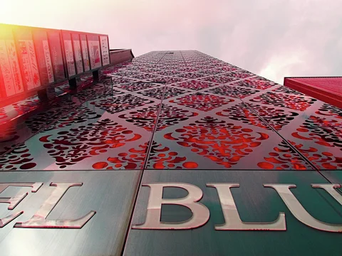 Repeating ornate red motifs cover a tall facade viewed upward beneath a pale pink sky.