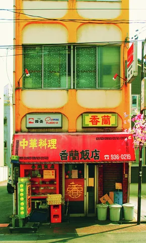 A narrow orange building has green upper windows and a red restaurant sign above a cluttered entrance.