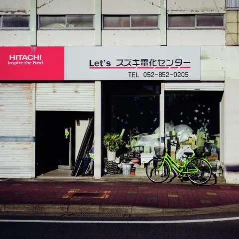 A green bicycle stands outside a cluttered shop window beneath a broad white sign and upper windows.