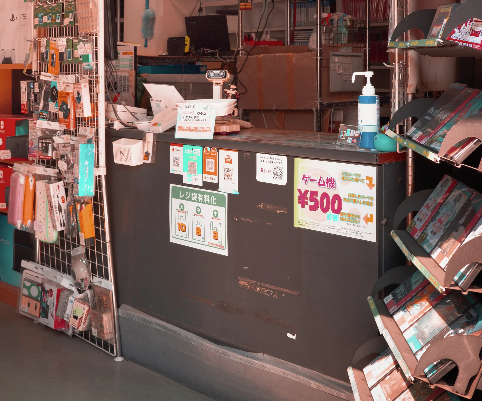 A shop counter holds sanitizer and price signs beside tightly packed displays of small merchandise.