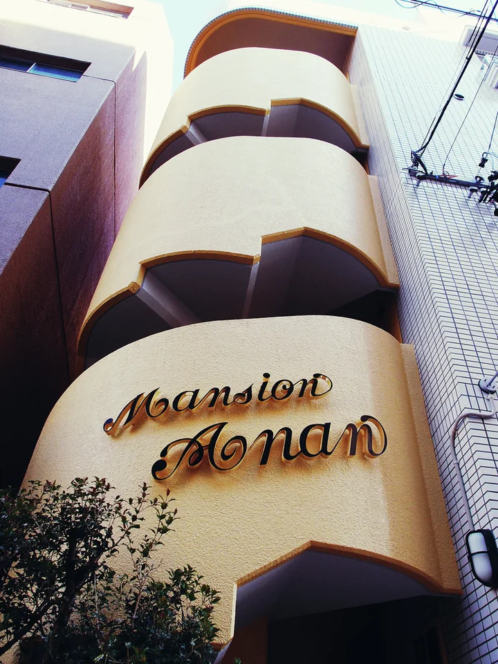 Rounded pale balconies rise above decorative Mansion Anam script on a narrow curved building facade.