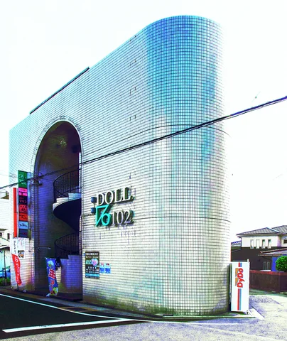A rounded silver-tiled building has a tall dark arched entrance and raised lettering beside a narrow road.