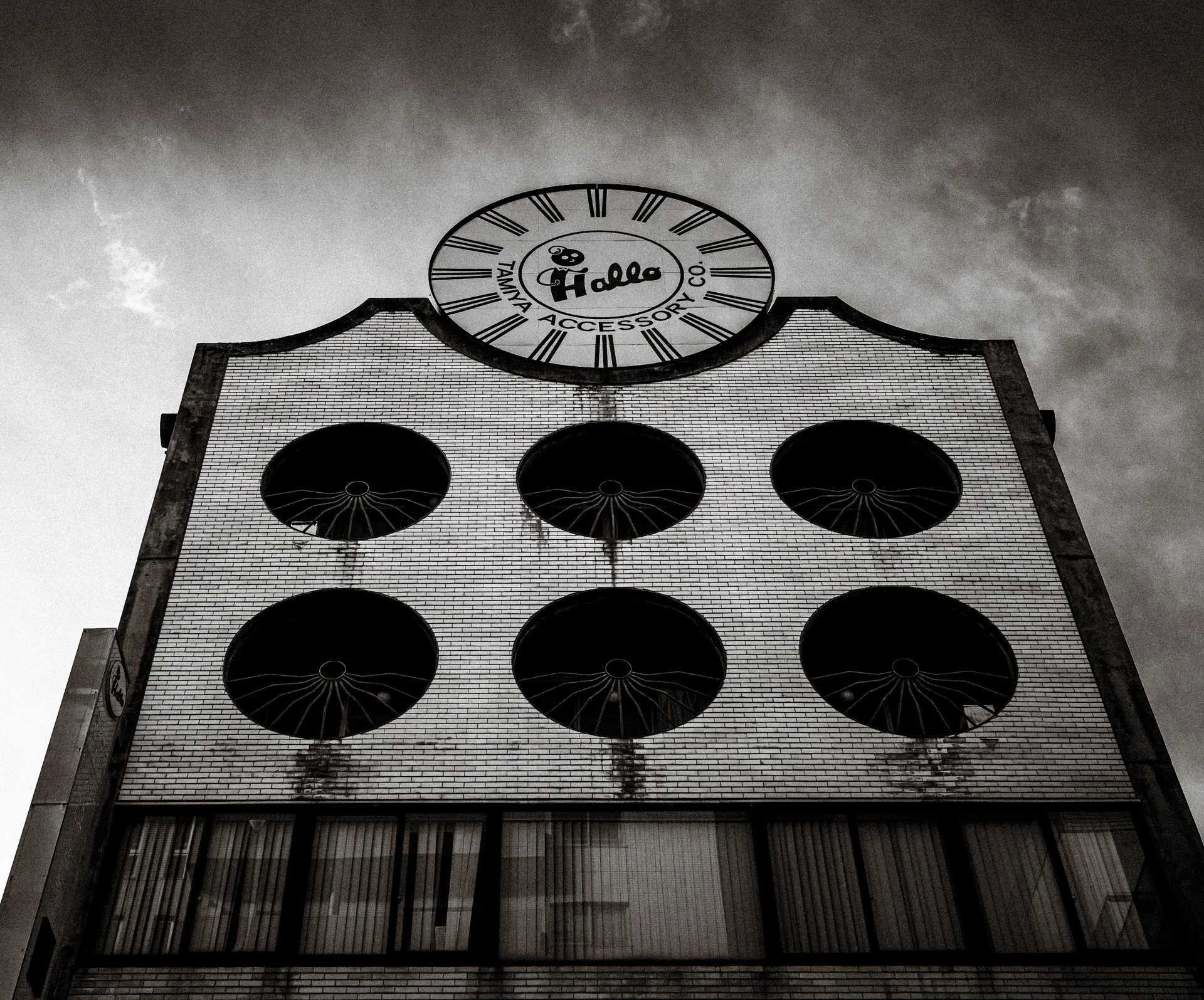 Six circular openings punctuate a brick facade topped by a decorative clock in a black and white view.