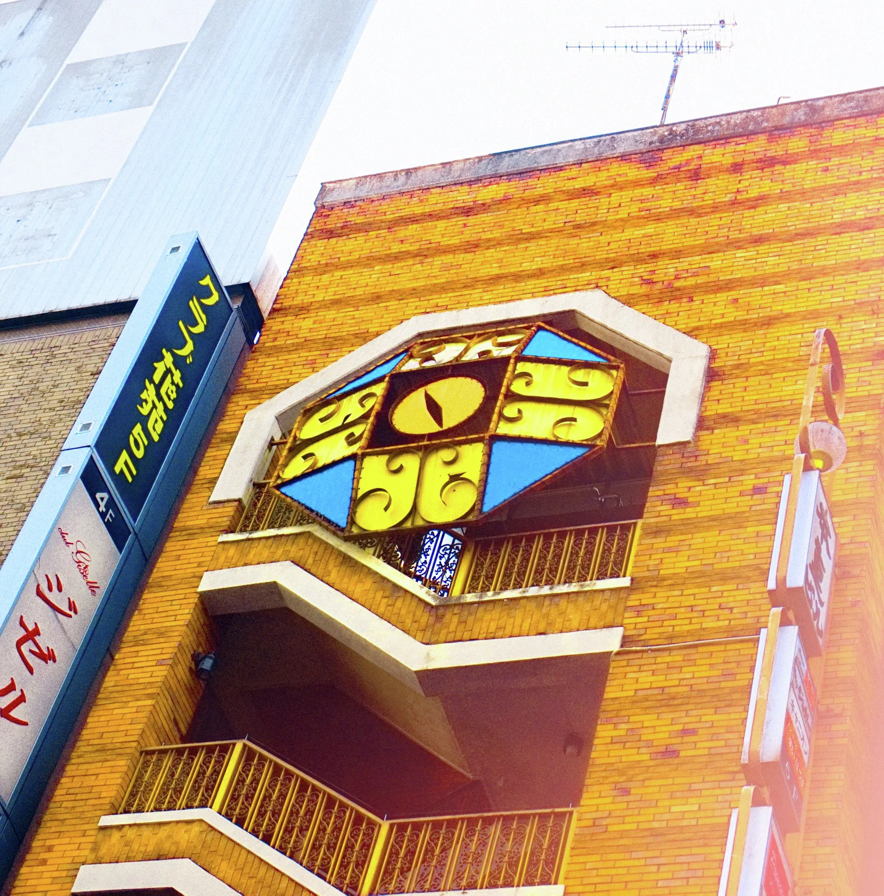 Angular outdoor balconies project from an orange brick facade beneath a colorful geometric cat-face sign.