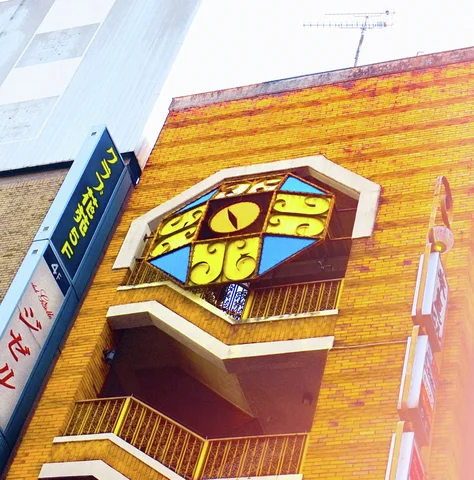 Angular outdoor balconies project from an orange brick facade beneath a colorful geometric cat-face sign.