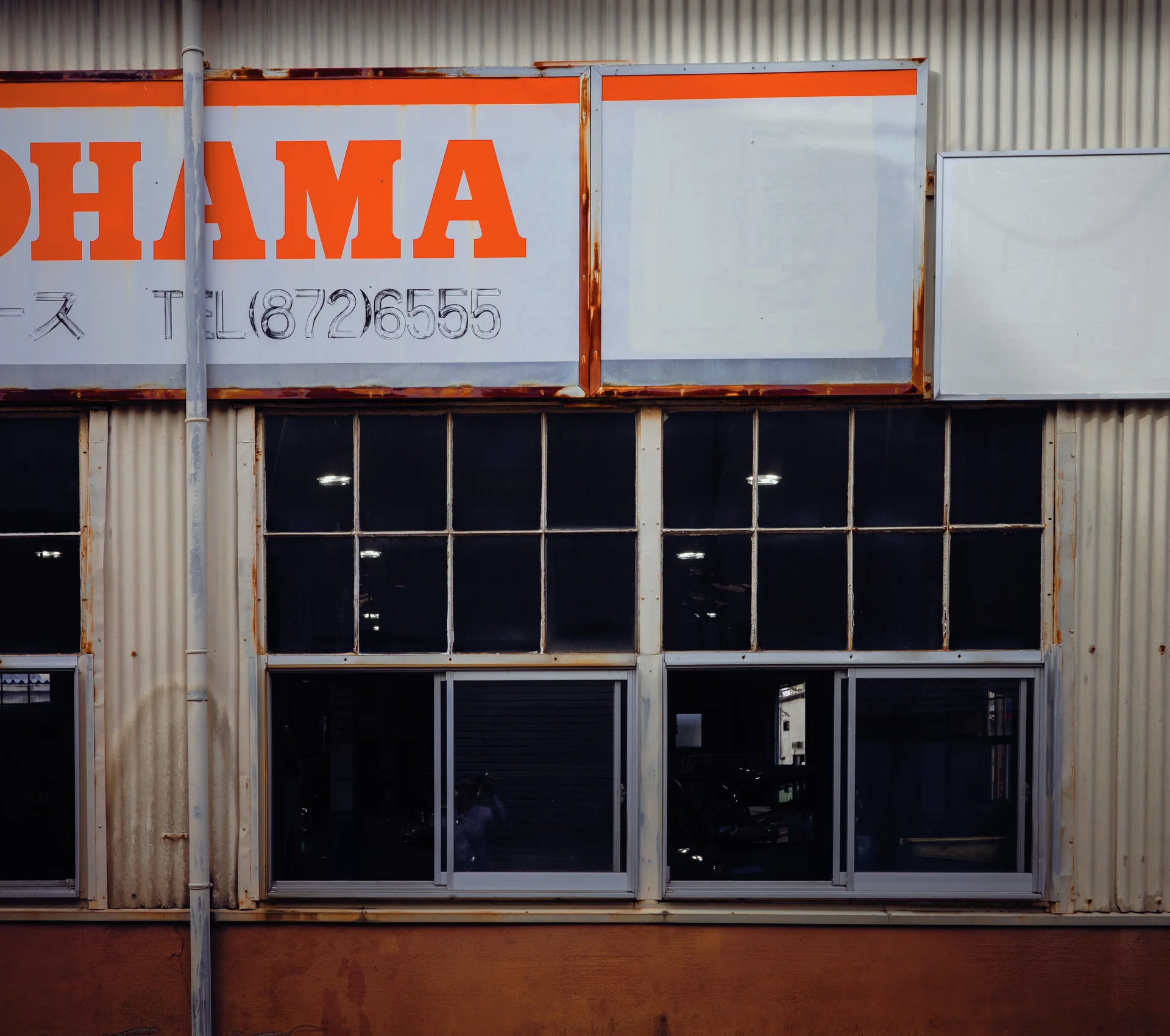 Large orange lettering tops a row of dark windows in a corrugated workshop facade.