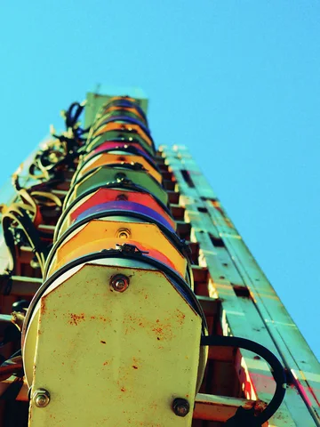 Rounded yellow sign panels and exposed metal brackets rise vertically against a bright turquoise sky.