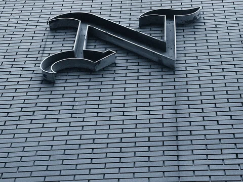 A large dark metal N emblem projects from a wall of narrow gray bricks.