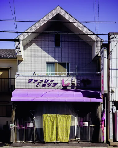 A narrow gabled building has a purple awning and pale yellow fabric hanging across its ground-floor frontage.