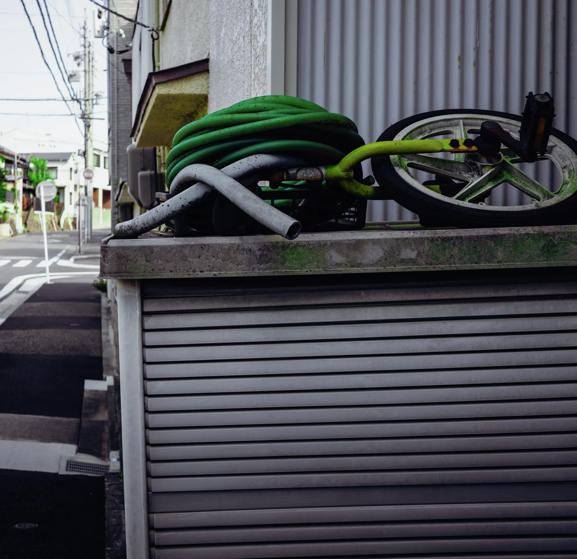 Coiled green hoses and a bicycle rest on a low structure above a closed metal shutter.