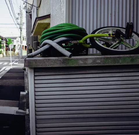 Coiled green hoses and a bicycle rest on a low structure above a closed metal shutter.