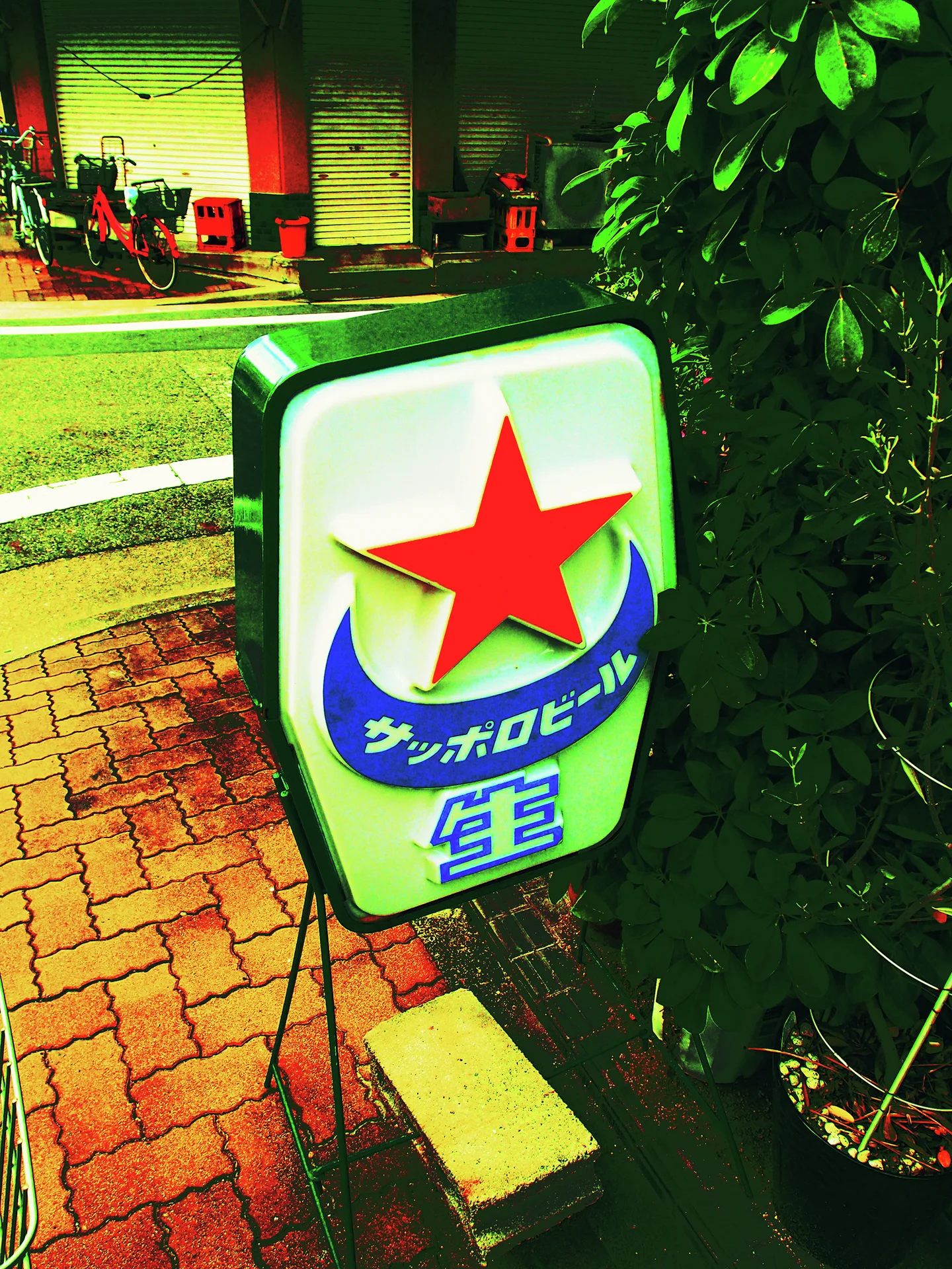 A freestanding sign with a large red star stands beside brick pavement and foliage.