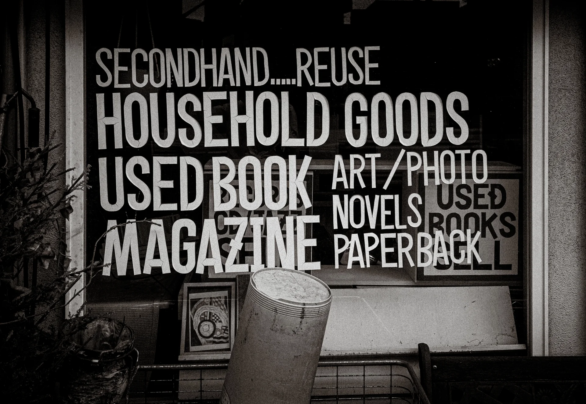 Large white English lettering advertising secondhand goods and books fills a dark shop window in black and white.