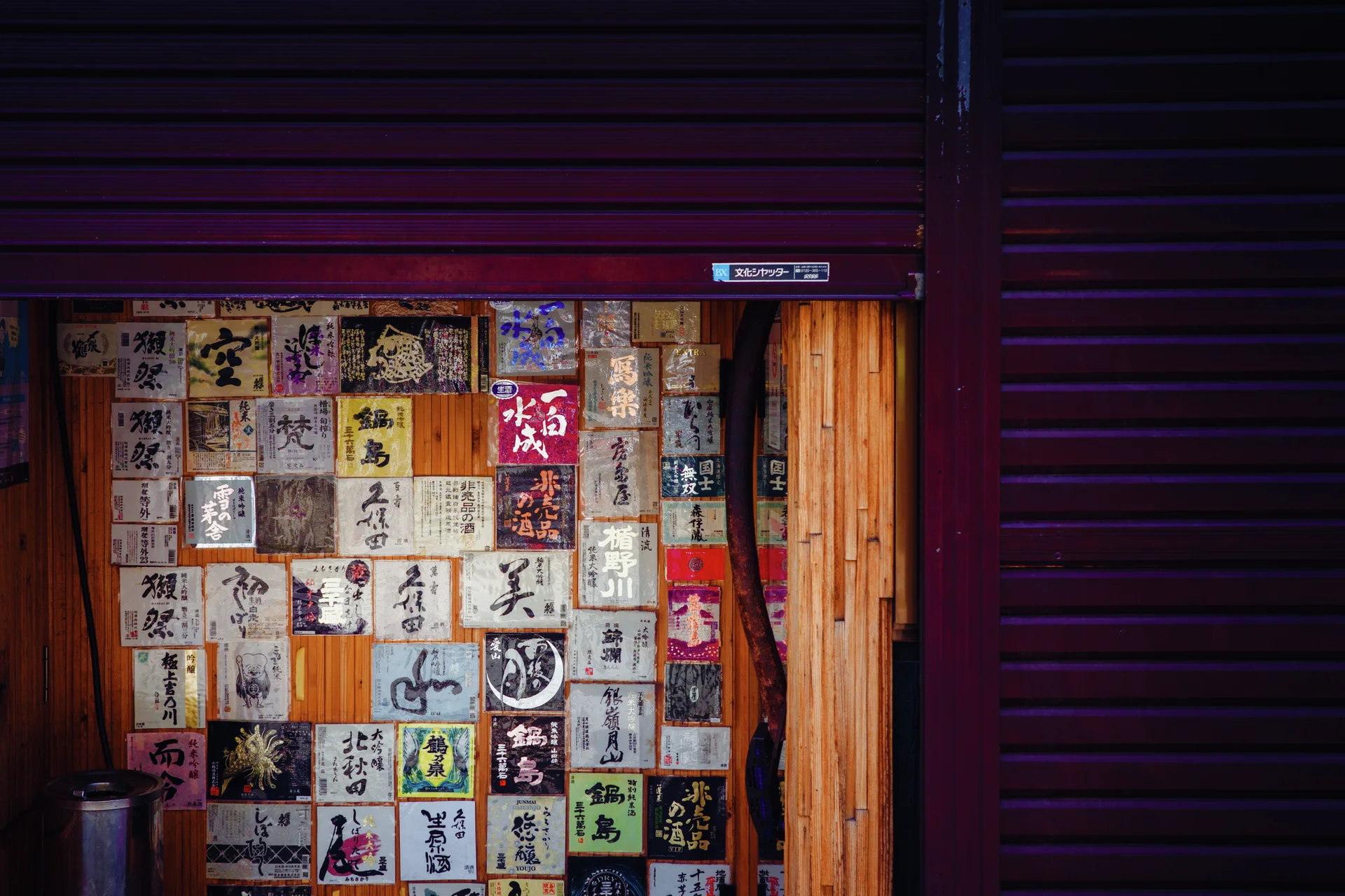 A patchwork of illustrated labels covers a wooden door beneath a partly lowered shutter.