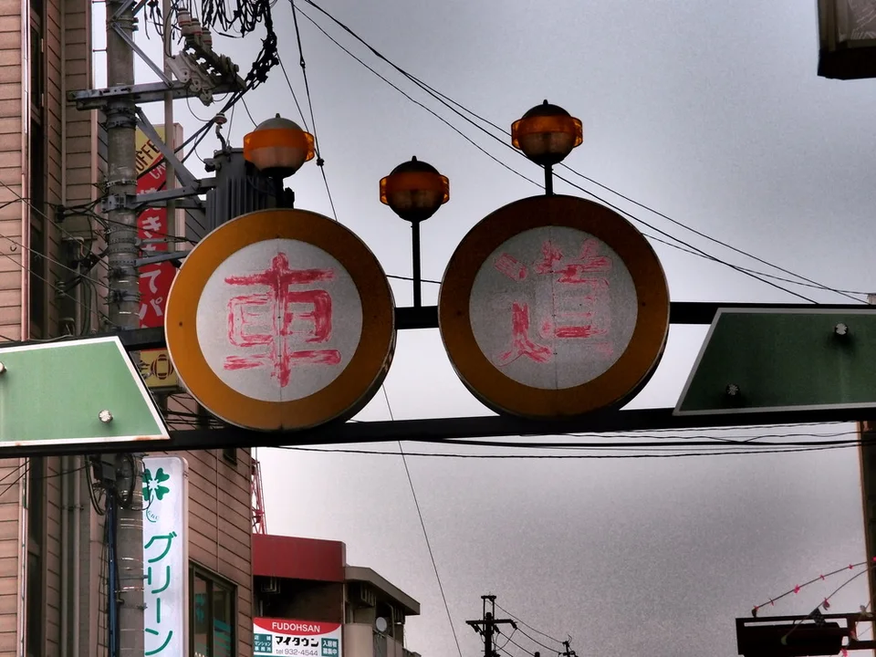 Two round signs with faded red characters hang beneath three orange lamps over a street.
