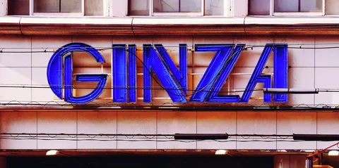 Large blue Ginza lettering projects from a pale tiled facade beneath a row of upper windows.