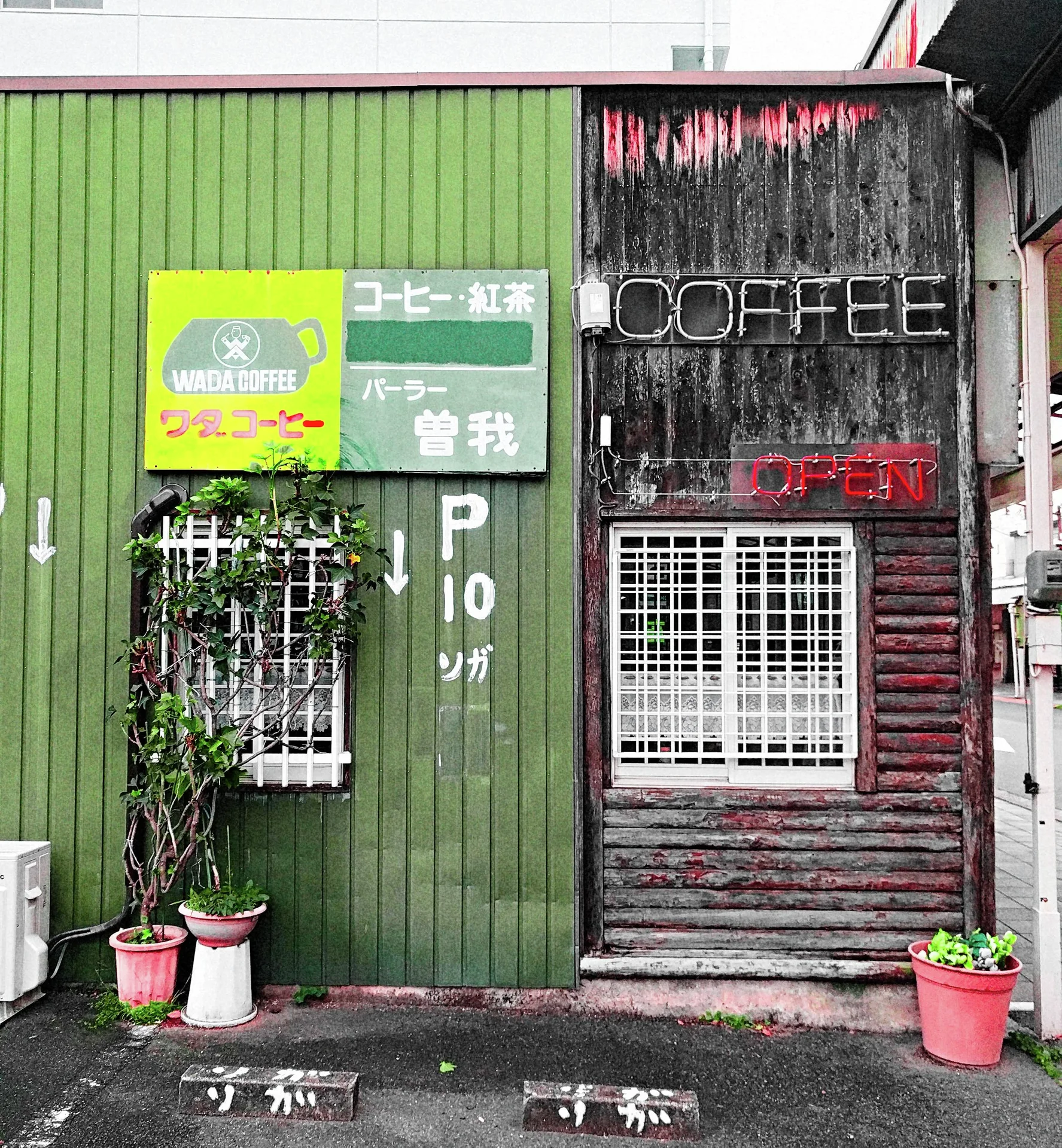 Potted plants stand before green siding and dark wooden panels with barred windows and Coffee lettering.