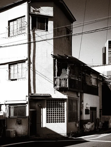 A narrow corner building has barred windows, glass blocks, and overhead wires in a black and white street view.