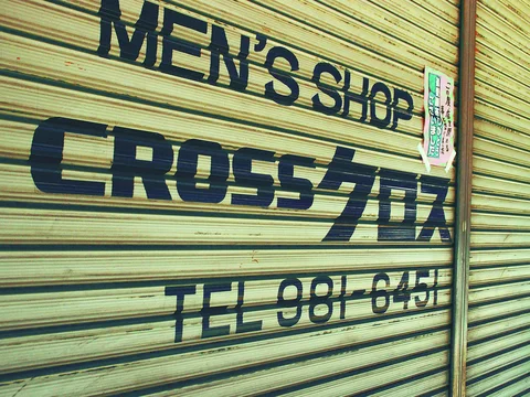 Bold dark MEN窶儡 SHOP and CROSS lettering covers a closed yellow-green metal shutter.