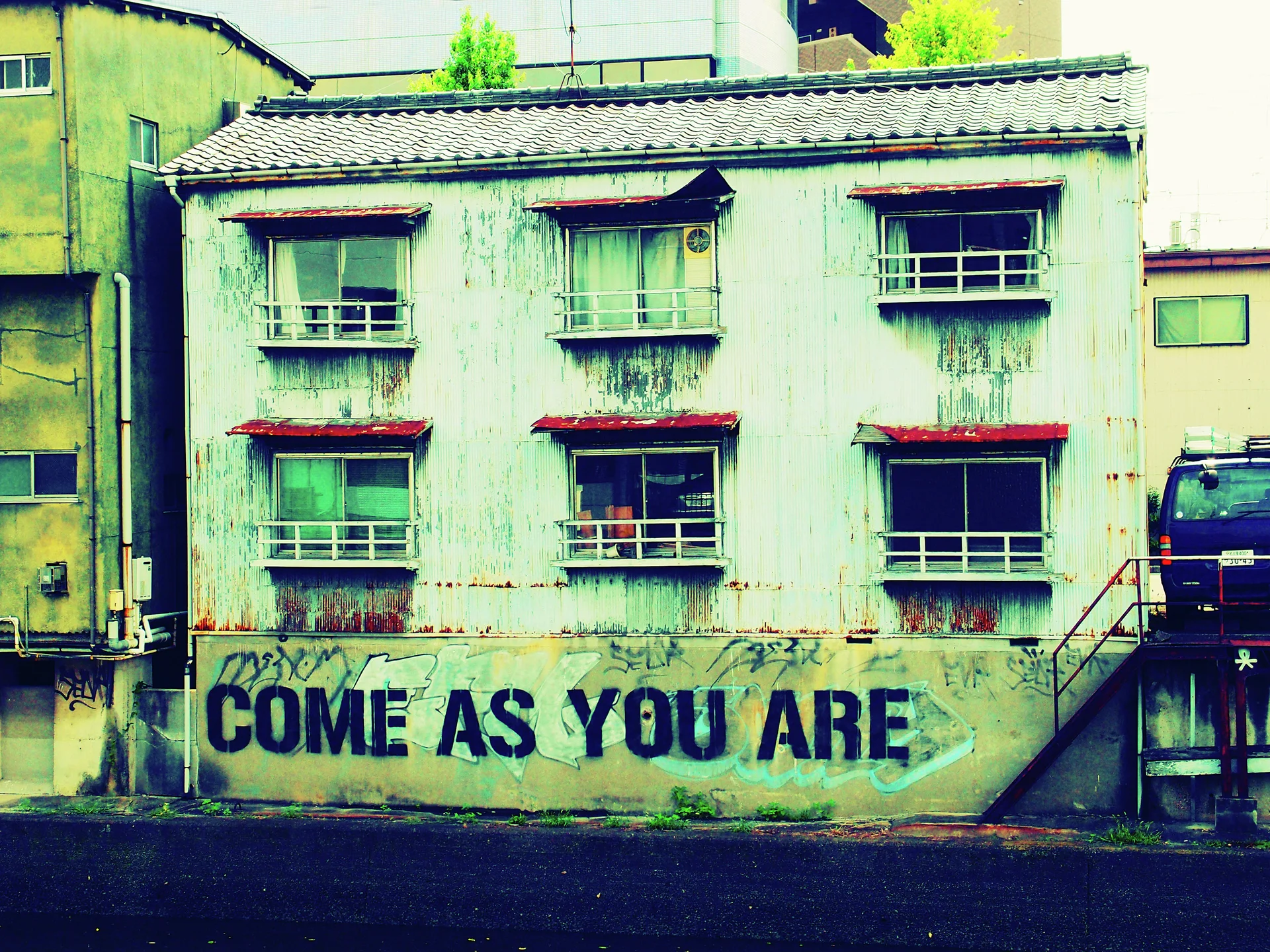 COME AS YOU ARE graffiti spans a weathered wall beneath rows of barred apartment windows.