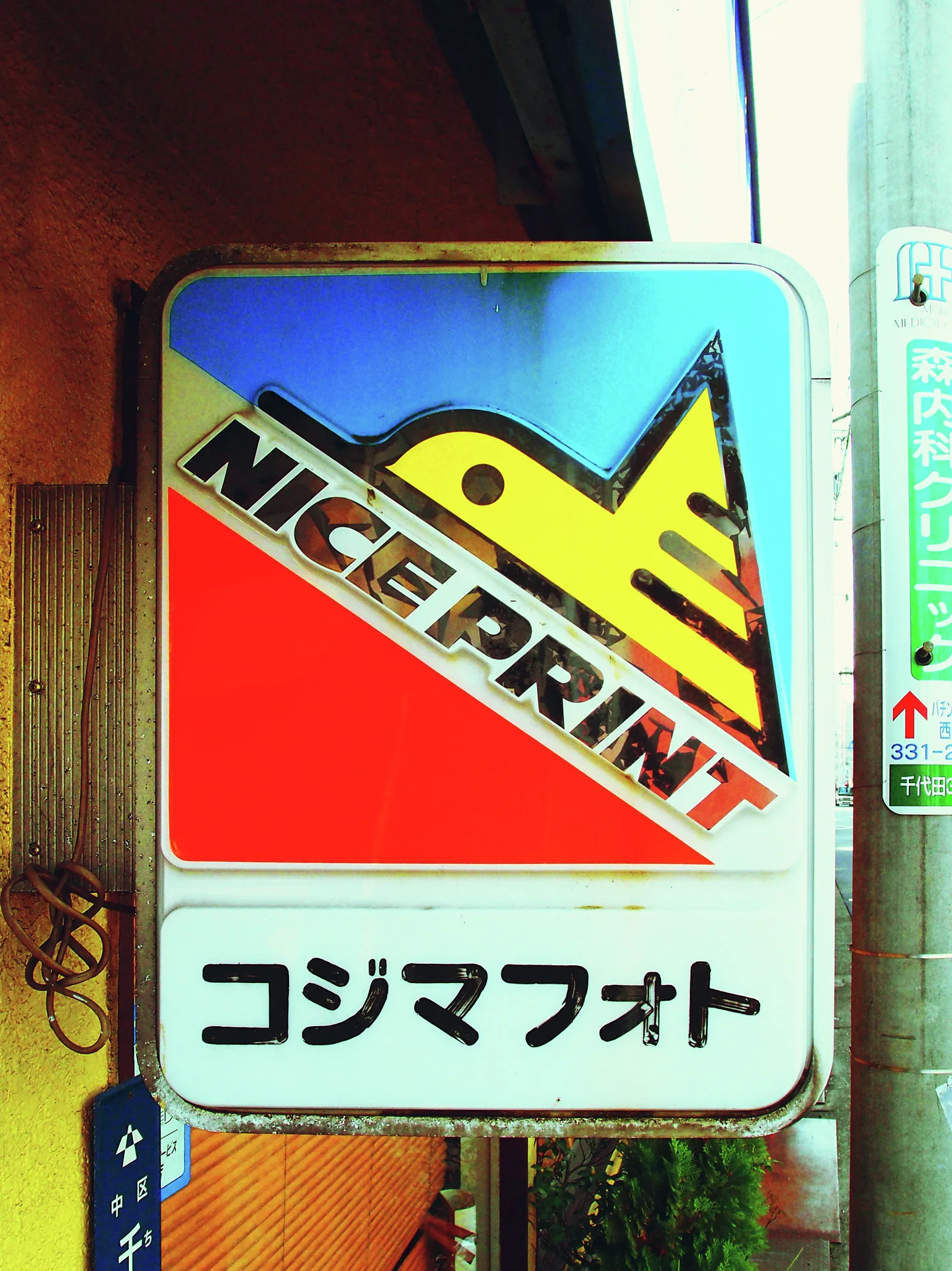 A colorful NICE PRINT sign with a stylized yellow bird projects beside a doorway.